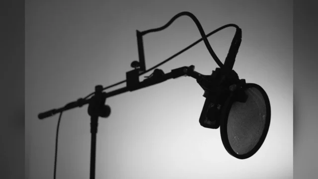 Black and white image of a professional studio microphone with a boom arm and pop filter.